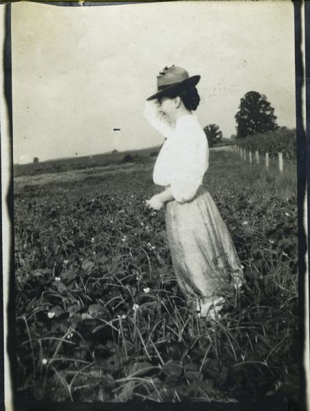 Stanta Bordner standing in a farm field and holding her hat on her head. Probably in Indiana.