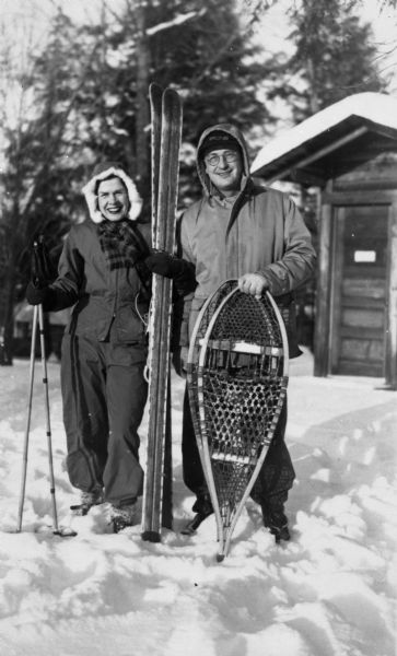 Winter scene with Mary and Nelson Ross of Ross' Teal Lake Lodge. They are posing in the snow with skis and snowshoes.