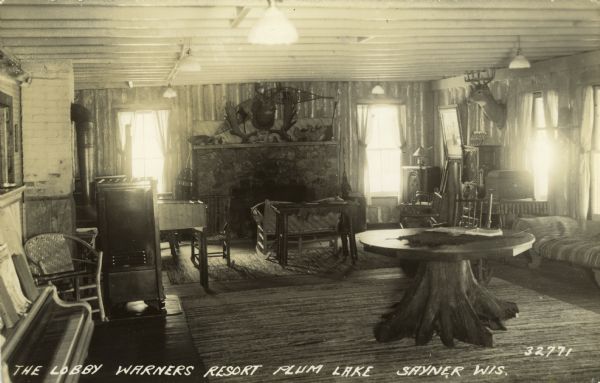 The lobby at the resort. There is a piano in the left foreground, and a large fireplace is along the back wall. Caption reads: "The Lobby at Warner's Resort, Plum Lake, Sayner, Wis."