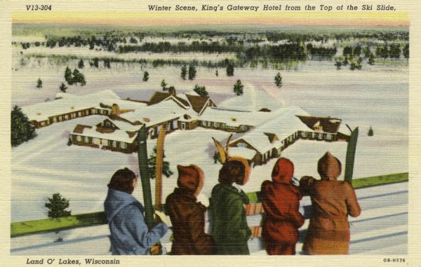 Five people are standing at a fence rail looking down at King's Gateway Hotel. Caption reads: "Winter View at King's Gateway Hotel from the Top of the Ski Slide, Land O'Lakes, Wis."