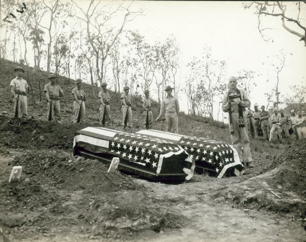 Military Chaplain Fred Bartrop performs an Episcopal burial ceremony for Byron Darnton over the coffins; Bomana Military Cemetery, Port Moresby, New Guinea.