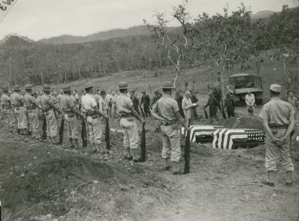 Darnton-Fahuestock funeral with a rifle squad at attention and two coffins draped with American flags, Bomana Military Cemetery in Port Moresby, New Guinea.