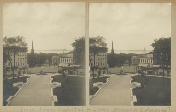 Stereograph view looking down North Hamilton Street from the State Capitol during the construction of the fourth capitol building. Features the Capitol Square sidewalk leading down North Hamilton Street businesses. Lake Mendota is on the horizon.
