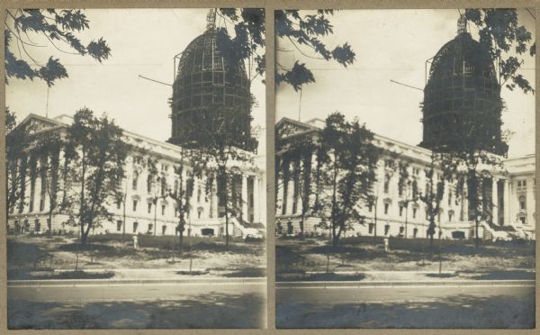 Stereograph view of construction of the Wisconsin State Capitol dome during the construction of the fourth capitol building. Features the Capitol Square sidewalk in the foreground. The dome is partially constructed, with metal girders showing its skeletal interior.