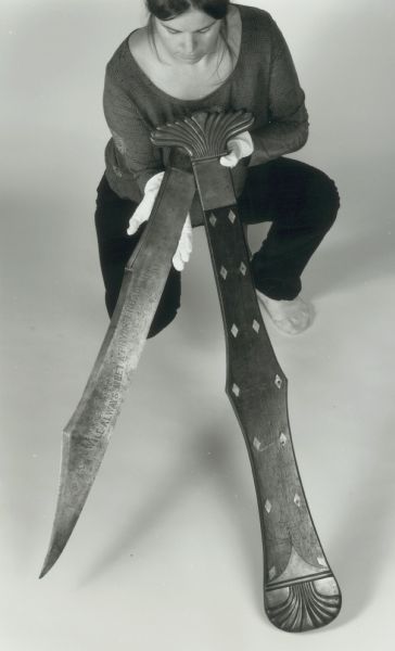 A woman holds the monster knife and its sheath. Giant knife presented to John Fox Potter by Missouri Republicans after Potter's threatened duel with a Virginia congressman, 1860.<p>(Museum object #1957.1122)</p>