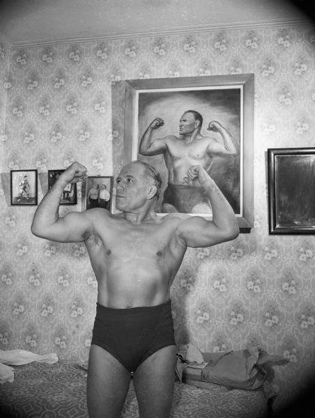 Local wrestler "Jimmy" Demetral poses flexing his muscles in front of a painting of himself.