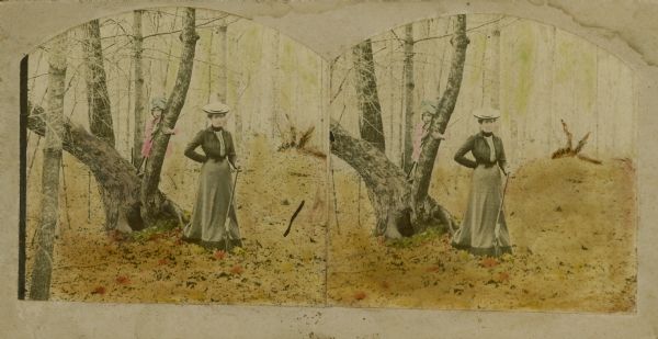 Hand-colored stereograph of Mattie Sprague Attoe Du Mond and her daughter, Maudie, near the fish pond on John O. Evan's farm. Mattie holds a rifle; Maudie stands on the trunk of a tree.