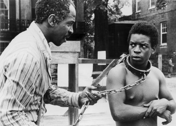 Scene from the popular television mini-series "Roots," showing actor LeVar Burton in chains portraying the slave Kunte Kinte, who had recently arrived on a slave ship from Africa, and Lou Gossett as the slave known as Fiddler.