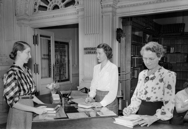 Close-up of the Library Circulation Desk and librarians Esther DeBoos and Margaret Gleason (right) behind the desk at the Wisconsin Historical Society.