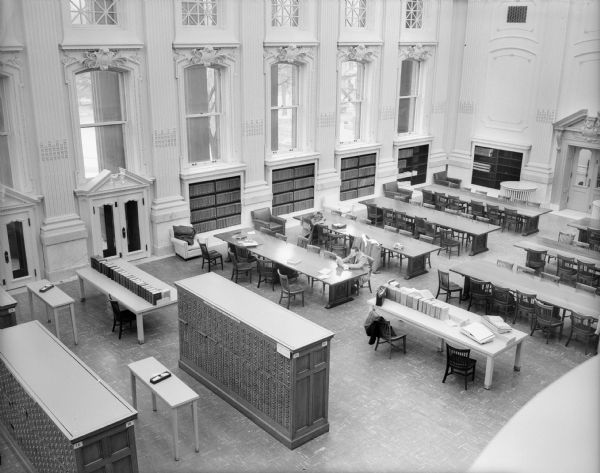 View of the Historical Society Library Reading Room taken from the Visitors Gallery.  Although undated, the photograph was probably taken shortly after the completion of remodeling in 1955. During this remodeling many of the original mahogany tables were eliminated, linoleum tiles replaced the original cork flooring, and the addition of overhead fluorescent lighting ended the need for the original brass table lamps.