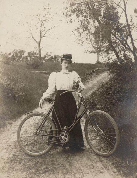 A woman stands with her bicycle on a country road.