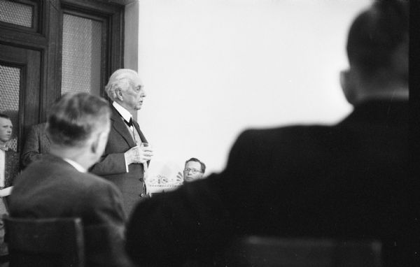 Architect Frank Lloyd Wright speaking at a hearing at the Wisconsin State Capitol. The hearing was held in the Education and Transportation Offices, room 314 NW of the Capitol. Wright testified before the Assembly Taxation Committee in favor of a bill granting tax-exempt status to Taliesin as a non-profit education institution.