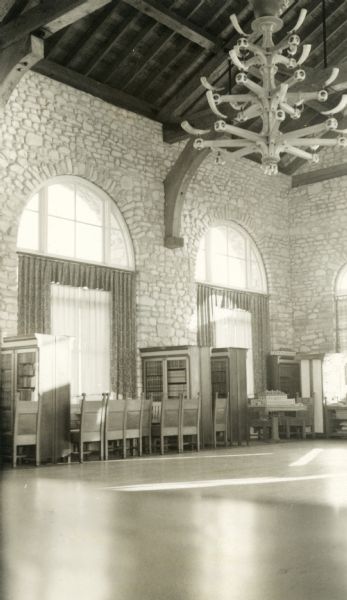 Interior view of the Thordarson library with bookcases and a spectacular chandelier with buffalo horns. The building is of stone, with arched windows.