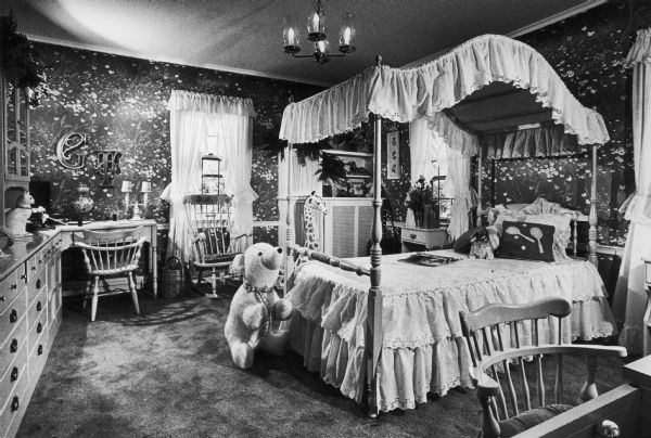 Interior view of a girl's bedroom, featuring a canopy bed and a stuffed bear doll.