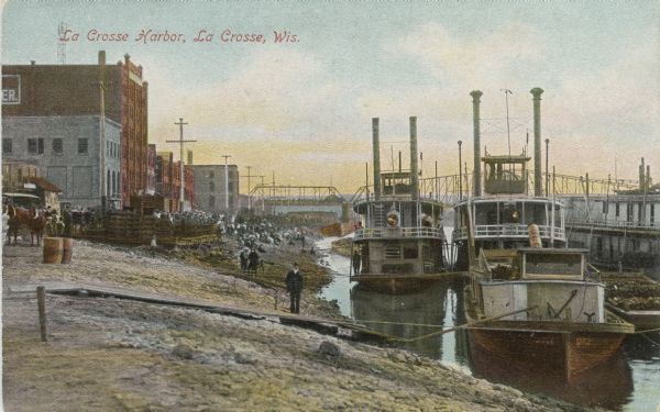 Harbor full of steamboats. The shoreline is bustling with people walking amidst the buildings, piers and bridges. Caption reads: "La Crosse Harbor, La Crosse, Wis."