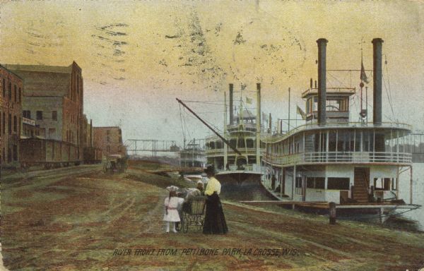 Caption reads: "Riverfront from Pettibone Park, La Crosse, Wis." There are three steamboats docked on the right in the harbor. A mother and her children are in the foreground and a horse-drawn vehicle is along the shoreline. On the left are commercial businesses and the railroad.