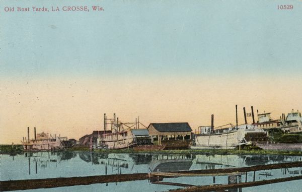 Old boat yards, with numerous steamboats, and buildings on the shoreline. Caption reads: "Old Boat Yards, La Crosse, Wis."