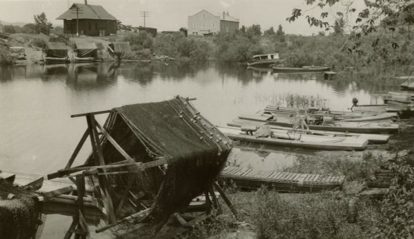 Fishing nets and implements and boats along the shoreline of the Mississippi River, with buildings visible in the background.