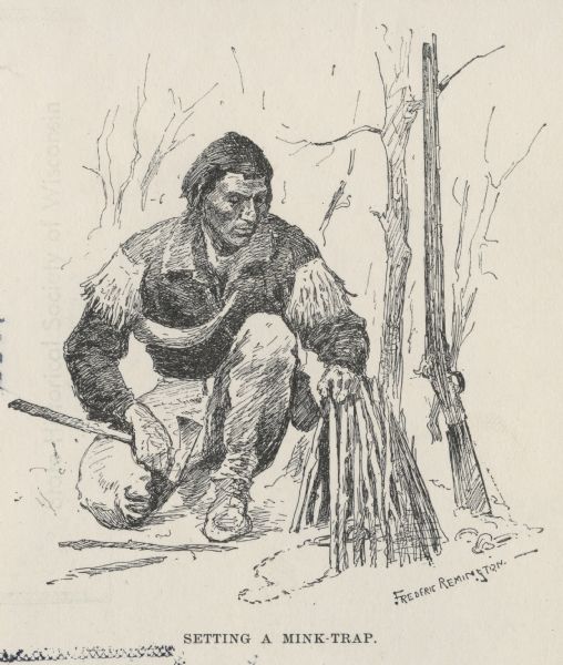 An Indian sets up a hunting trap, with a rifle resting against a tree in the background.