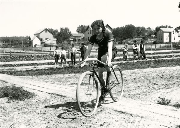 A man on a track bicycle in the foreground with spectators in the background.