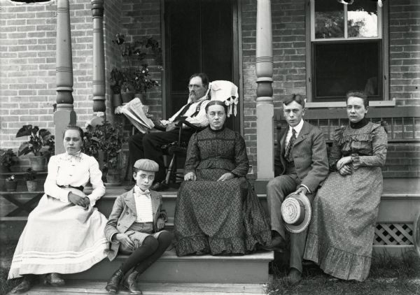 A family portrait on the front porch of their house. There are three females and three males.