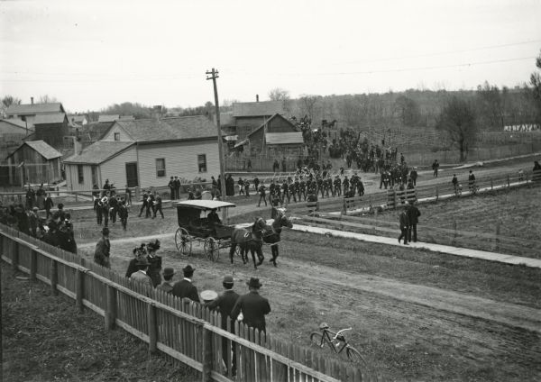 A small crowd watches as parading soldiers march down the street.