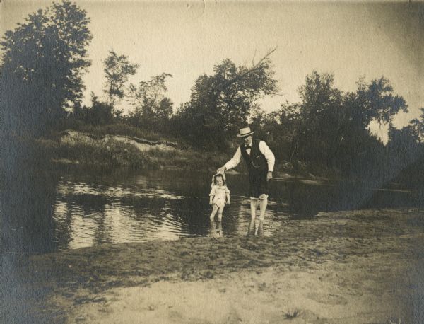 A father and young child are wading in a river.
