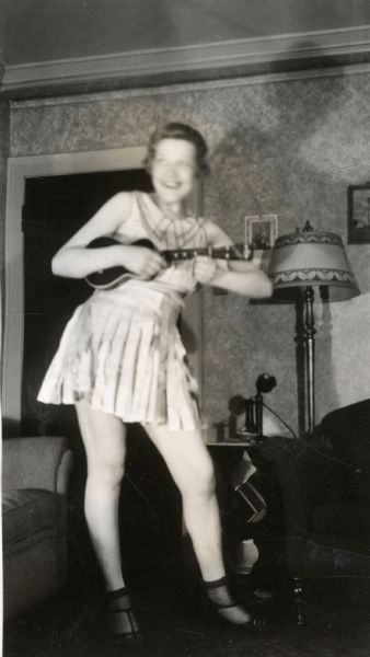 A woman with a ukulele in a household setting.