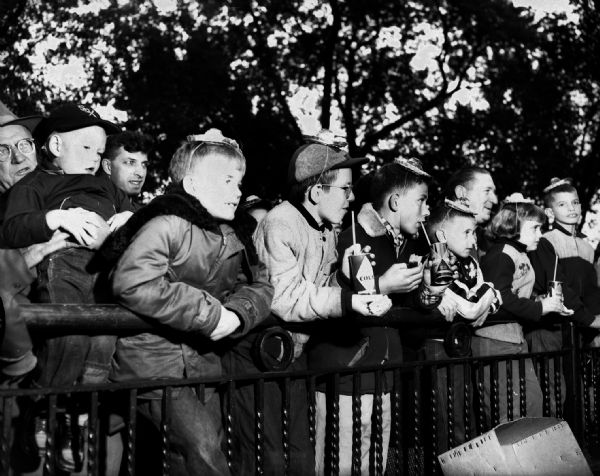 Children leaning against a fence at the fifth adoptive birthday party for Samson and Sambo at the Washington Park Zoo. Several of the children are drinking out of cola cans. The party was sponsored by Pabst Sparkling Beverages.