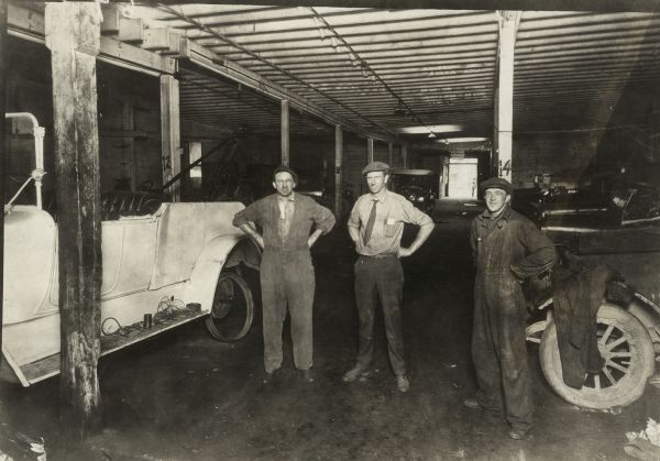 Three men standing in front of vehicles inside Theodore O. "Ted" Helleckson's first automobile repair shop in Madison, the West Side Garage, at 621 University Avenue. Ted is on the left; his partner and Secretary-Treasurer of the company, Ralph S. King, is in the middle. Their second business venture was the King and Helleckson Service Station at 1002 South Park, on the southeast corner of the intersection of South Park Street and Fitchburg (now Fish Hatchery Road).