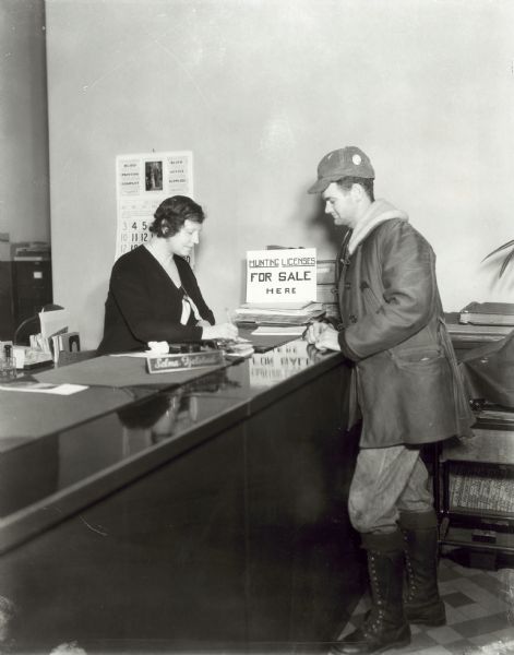 Man at the counter of office in Dane County where clerk, Selma Fjelstad, is issuing a hunting license.