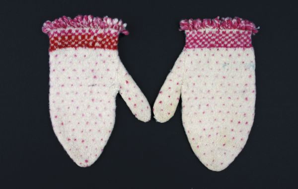 Baby mittens knitted of ecru, red and pink wool yarn.
