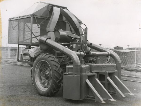 View of a 2-row cotton picker mounted on a Farmall tractor and parked in front of what apears to be a storage yard.