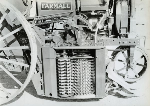Engineering photograph of an experimental one-row, single drum, small Farmall cotton picker attachment.  With the door removed, the picker drum and doffer units, along with the raising and lowering mechanism, are visible. The machine is attached to a Farmall tractor.