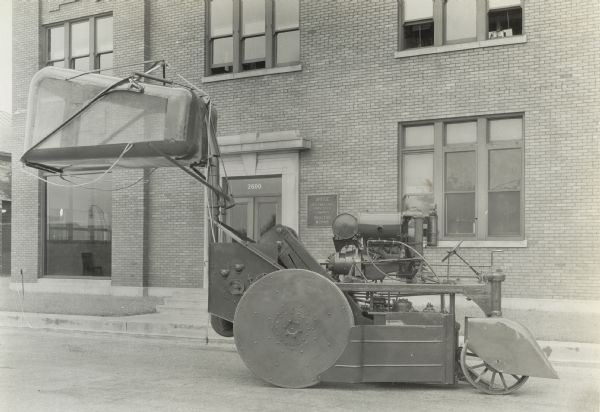 Engineering phtoo of an experimetnal single-row, two drum, self-propelled cotton picker. The photograph was taken outside International Harvester's Tractor Works office and shows the right side of the machine with the cotton container in the unloading position.