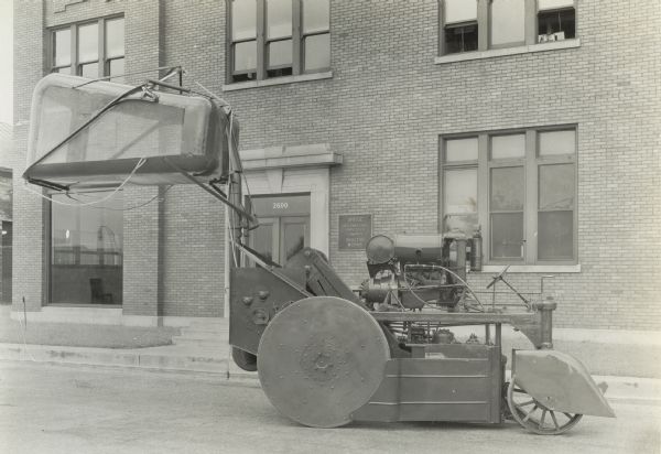 Engineering phtoo of an experimetnal single-row, two drum, self-propelled cotton picker.  The photograph was taken outside International Harvester's Tractor Works office and shows the right side of the machine with the cotton container in the unloading position.