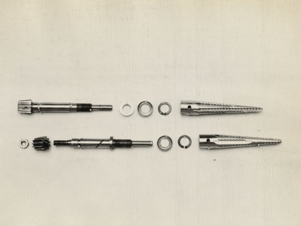 Engineering photograph of two cotton picker fingers, an integral gear with shielded washer and a threaded gear and shielded lockwasher.