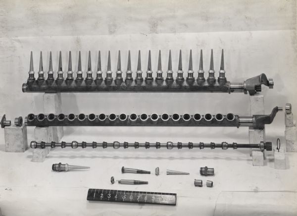 Engineering photograph of parts from a cotton picker lined up against a white background with a ruler to show their measurements.