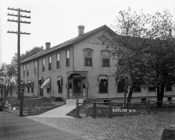 The first Klinkert Hotel. It burned down around 1905, and was replaced by the brick structure with the same name. Signs advertising Harper Rye are on either side of the door, and two liquor signs are displayed on the windows. A man is standing behind the front door.