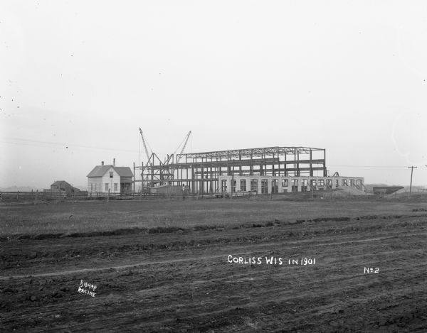 View from a distance of the framework of a large building under construction next to a house in Corliss.
