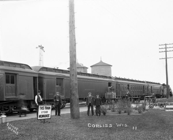 Train depot workers pose in front of a train at the depot. There is a sign that reads "This Train For Milwaukee".