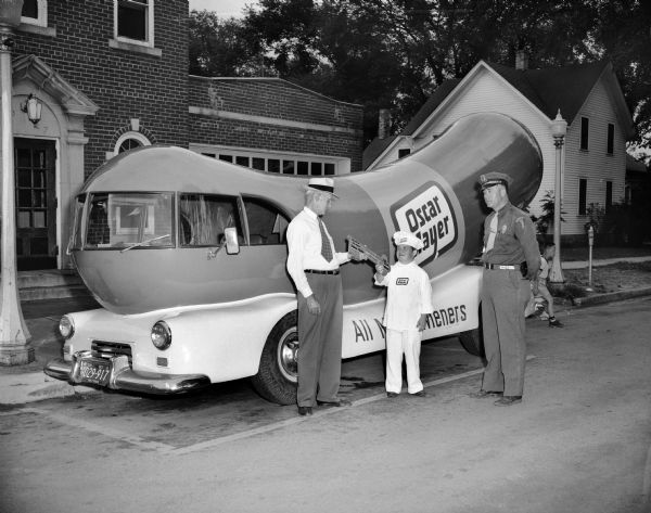 Meinhardt Raabe, dressed as Little Oscar, receiving the key to the city of Wisconsin Dells, while standing in front of the Wienermobile. Written on the key: "His Honor The Mayor Thomas J. Howley, Wisconsin dells, Wisconsin, Little Oscar 1955."
