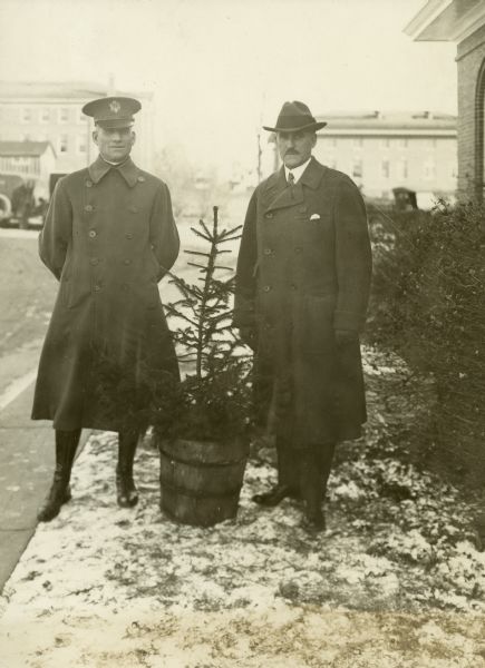 John S. Donald and an officer in uniform standing next to a potted evergreen tree.