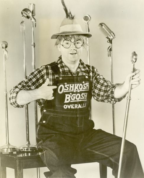 Radio announcer Johnny Olson wearing a pair of Oshkosh B' Gosh overalls. Olson hosted the "Oshkosh B' Gosh" Radio Program broadcast on stations WTMJ (Milwaukee), WSAU (Wausau)  and WTAQ (Eau Claire) in the late 1930's.