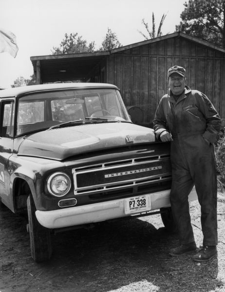 Actor John Wayne standing next to an International 1000B truck. He may be on the set of a production titled "Hellfighters."