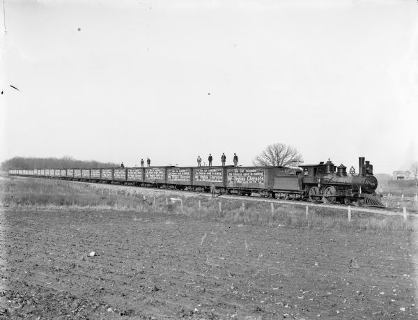 Men standing on top of, and around, a train carrying tobacco. A sign on the side of each car reads, "This car contains tobacco used in making Old Virginia Cheroots. Over one hundred million sold every year." There is a harvested field in the foreground and a farmhouse in the distance.