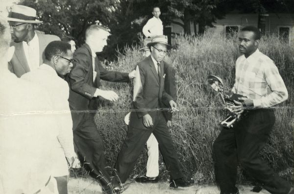 Violence against African American journalists covering the Little Rock integration story. Here the crowd moves in on Jimmy Hicks (center, wearing a hat), the managing editor of the <i>New York Amsterdam News</i>. The photographer is Earl Davy of the <i>Arkansas State Press</i>. A few minutes later both men were beaten and Davy's camera smashed. Hicks was slugged from behind moments after the photograph was taken.