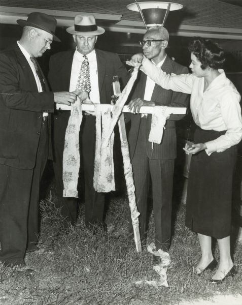 Daisy and L.C. Bates with two men and a Ku Klux Klan (KKK) cross that they found in their yard. Because this event preceded the integration crisis of 1957 in which the couple took a leading role, it is likely this racial harassment was aimed at their crusading newspaper, the "Arkansas State Press." The two men are presumably police investigators.