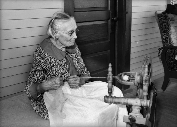 Side view of German grandmother using spinning wheel to spin yarn.