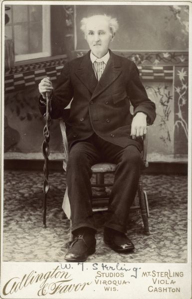 Carte-de-visite of William Triggs Sterling sitting in a chair and holding an ornate walking stick in front of a painted backdrop.